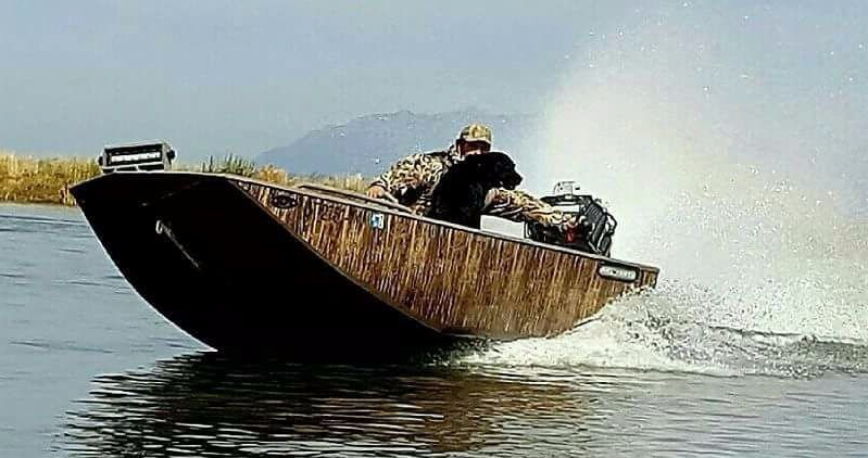 widowmaker 2048 hybrid V mud boat with camo wrap and a black labrador cruising through the water